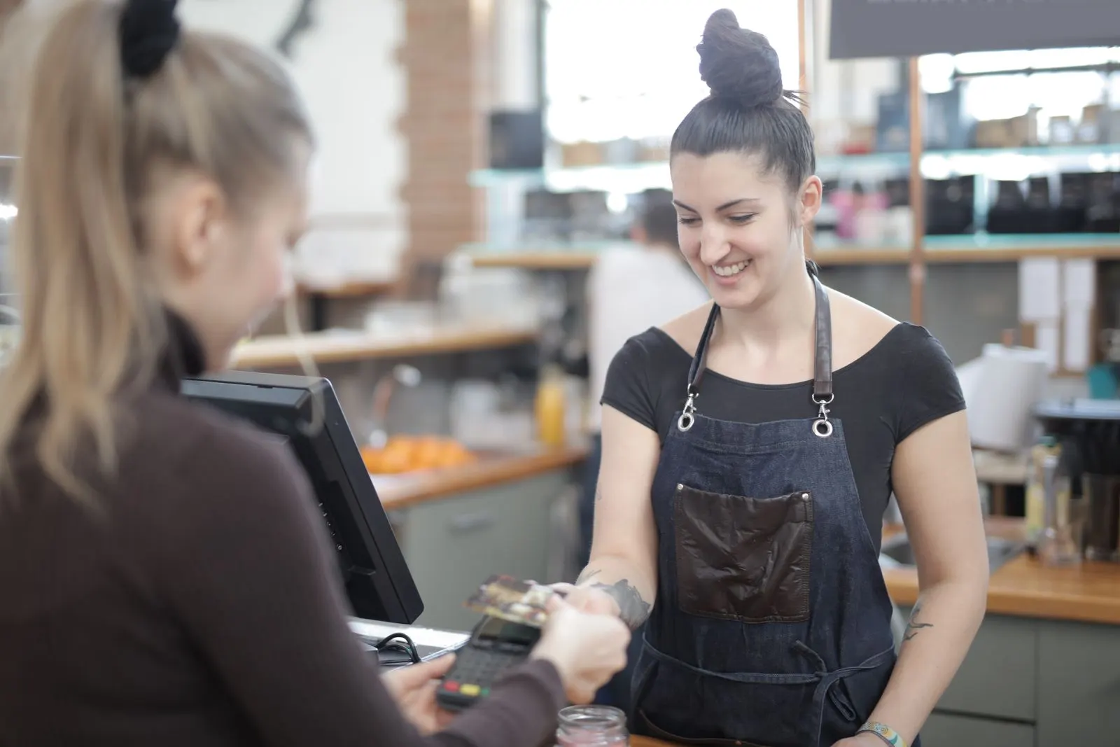 A cashier smiles while a customer pays by card at the counter